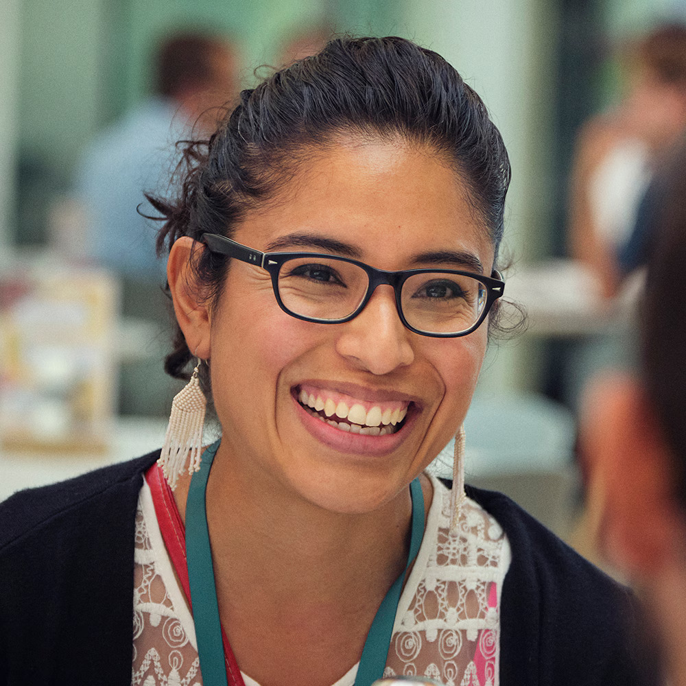 A woman wearing glasses smiles warmly at a man sitting at a table.